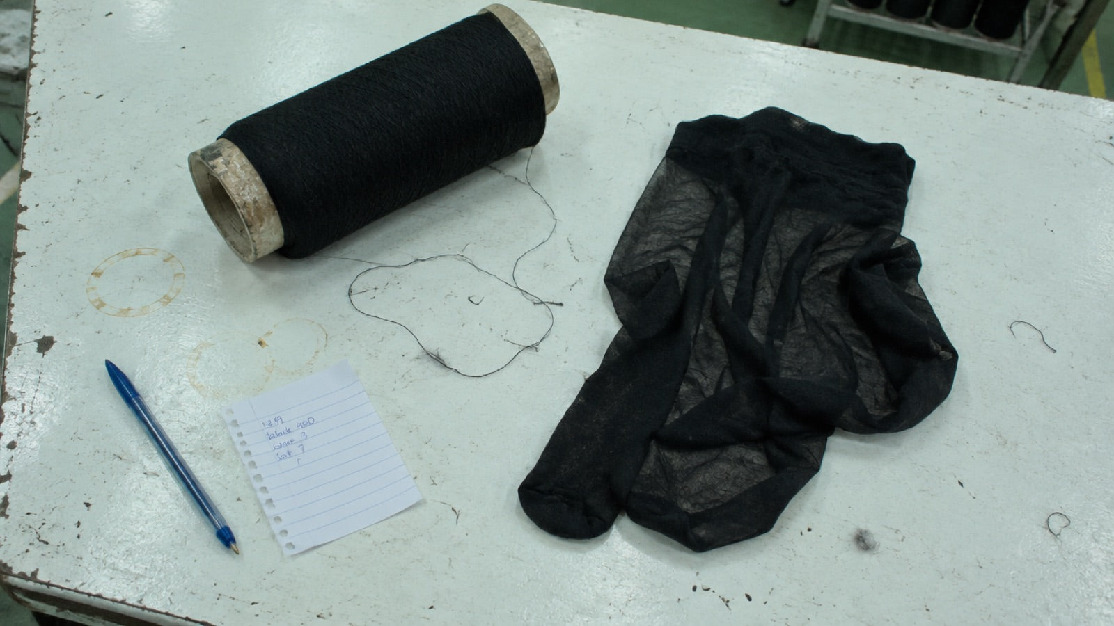 A cone of black nylon yarn and a folded pair of sheer tights on a worktable in the hosiery factory